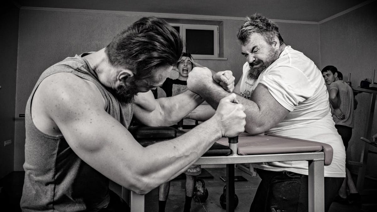 Dramatic black and white arm wrestling scene with muscular men indoors.